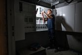 Une personne travaille sur un panneau électrique éclairé par une lampe de travail sans fil.