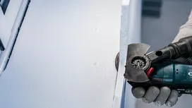Une personne portant un équipement de sécurité utilise un outil électrique pour couper une feuille d’isolant.