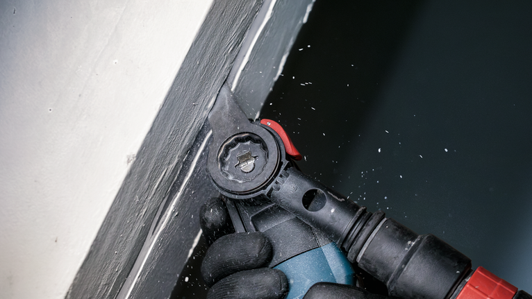 Une personne portant un équipement de sécurité utilise un outil électrique pour poncer la peinture près d'un coin de mur.