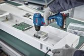 Une personne portant un équipement de sécurité utilise une perceuse sans fil pour assembler des composants électroniques.