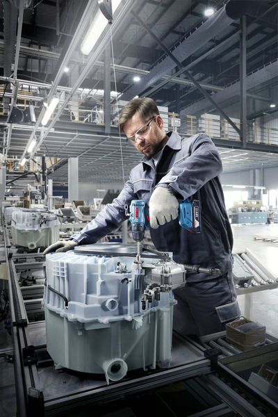 Une personne portant un équipement de sécurité utilise une perceuse sans fil pour assembler des machines dans une usine.