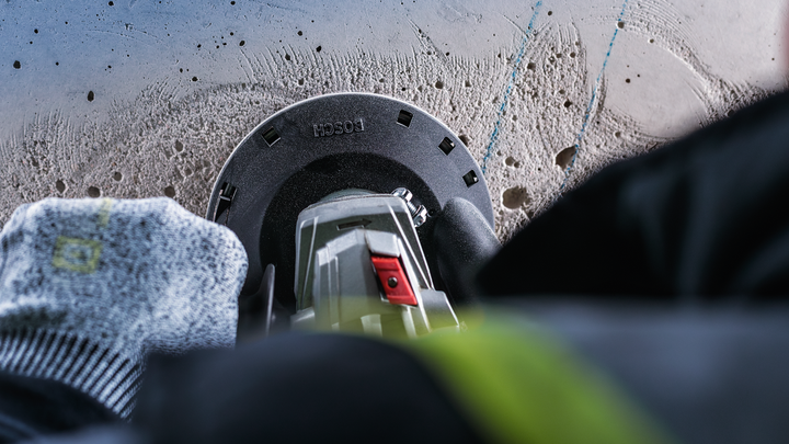 Un ouvrier portant un équipement de sécurité perce du béton avec un outil électrique.