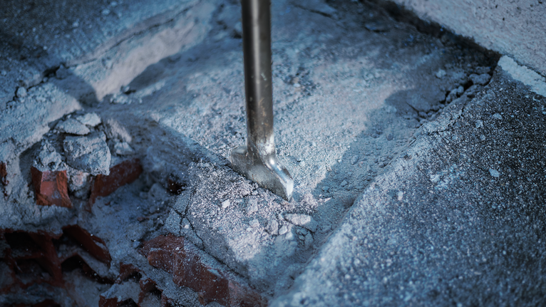 Ciseau cassant le béton, dispersant la poussière et les débris.
