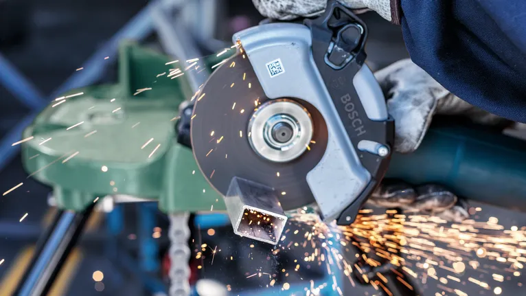 Une personne portant un équipement de sécurité coupe un tuyau métallique avec une scie circulaire, créant des étincelles.