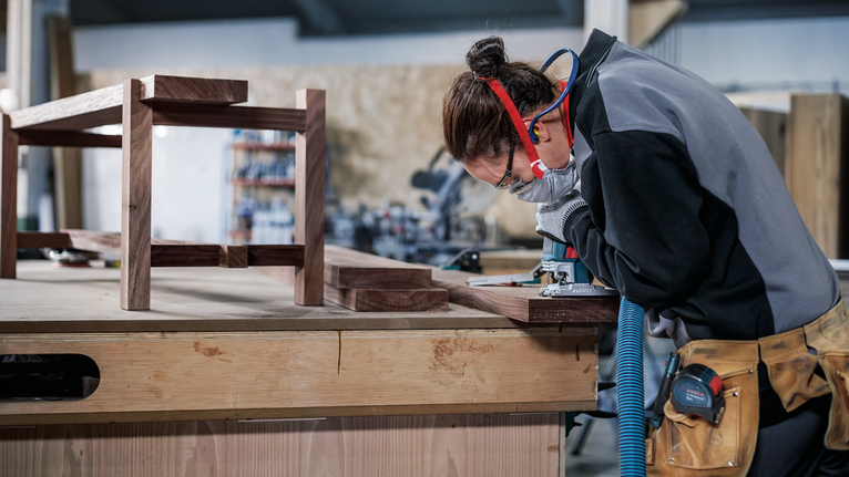 Une personne portant un équipement de sécurité ponce une planche de bois dans un atelier.