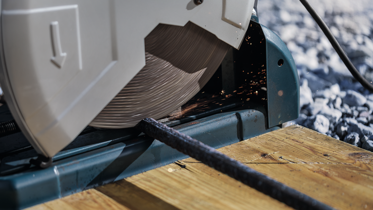 Scie à tronçonner coupant une tige métallique sur une surface en bois.