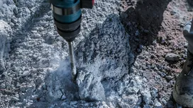 Un marteau perforateur brise des gravats de béton à proximité d'une personne portant un équipement de sécurité.