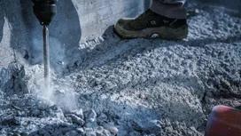 Une personne portant un équipement de sécurité perce du béton le long d'un mur.