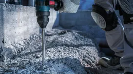 Une personne portant un équipement de sécurité perce du béton sur un chantier de construction.