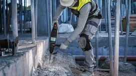 Une personne portant un équipement de sécurité utilise un outil électrique pour casser du béton.