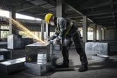 Une personne portant un équipement de sécurité utilise une meuleuse d'angle sur un conduit métallique sur un chantier de construction.