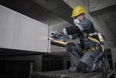 Une personne portant un équipement de sécurité broie du béton avec un outil électrique sur un chantier de construction.