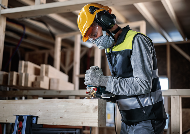 Une personne portant un équipement de sécurité utilise une scie sauteuse pour couper du bois dans une zone de construction.
