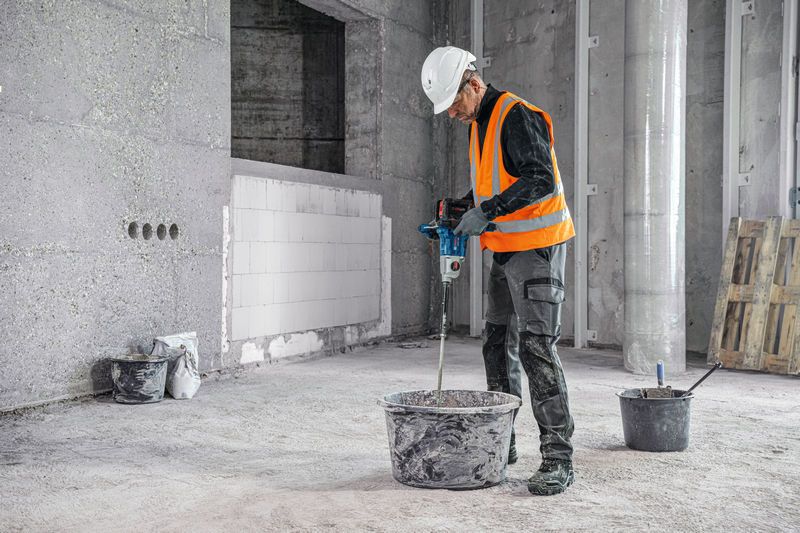 Une personne portant un équipement de sécurité mélange des matériaux à l'aide d'un mécanisme d'agitation sur un chantier de construction.