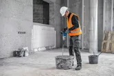 Une personne portant un équipement de sécurité mélange des matériaux à l'aide d'un mécanisme d'agitation sur un chantier de construction.