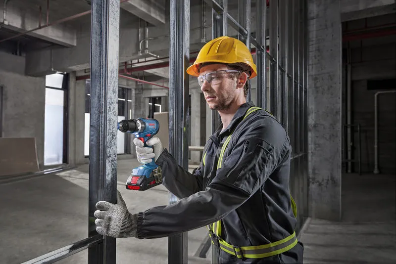 Une personne portant un équipement de sécurité perce une charpente métallique sur un chantier de construction.