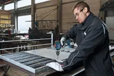 Une personne portant un équipement de sécurité perce un treillis métallique sur un établi dans une usine.