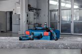 Ponceuses orbitales aléatoires sans fil et un boîtier bleu placés sur une surface en béton dans un atelier.