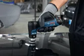 Une personne portant un équipement de sécurité utilise une ponceuse sans fil pour polir la surface d'une voiture.