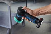 Une personne tient une polisseuse sans fil avec un tampon en mousse verte près d'un chariot en métal.