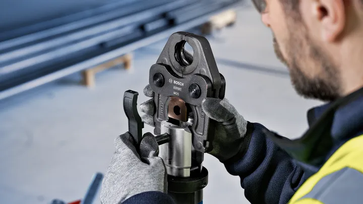 Une personne portant un équipement de sécurité utilise un outil de sertissage sur un tuyau métallique.