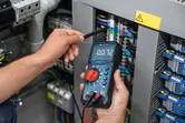 Une personne mesure la tension sur un panneau électrique à l’aide d’un multimètre numérique.
