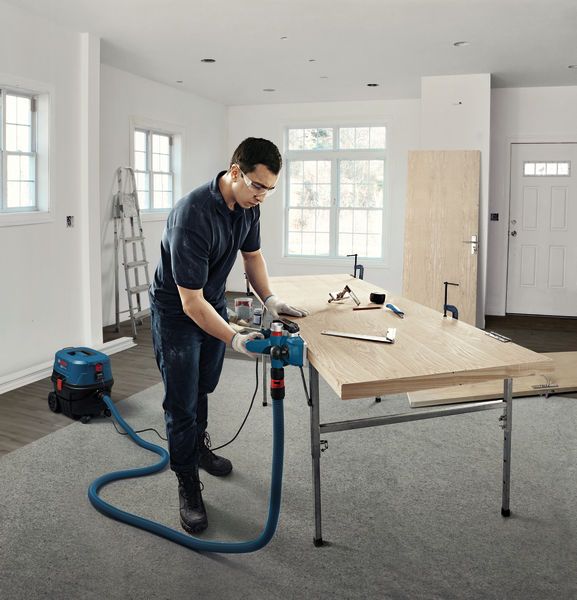 Une personne portant un équipement de sécurité utilise une raboteuse sur une planche de bois dans un atelier.