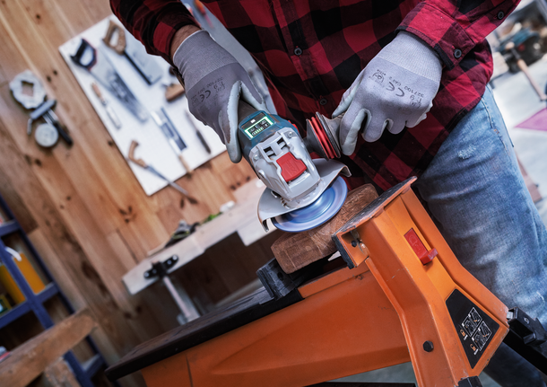 Une personne portant un équipement de sécurité utilise une meuleuse d'angle pour poncer du bois fixé sur un établi.