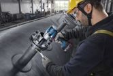 Une personne portant un équipement de sécurité serre des boulons sur des tuyaux industriels à l'aide d'une clé à chocs sans fil.