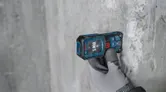Une personne portant un équipement de sécurité utilise un télémètre laser contre un mur en béton.