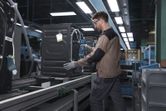 Une personne portant un équipement de sécurité fixe un appareil sur une chaîne de montage à l'aide d'un outil électrique.