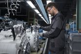Une personne portant un équipement de sécurité assemble des pièces de machines à l’aide d’un outil électrique sans fil.