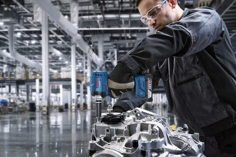 Une personne portant un équipement de sécurité utilise une perceuse sans fil sur une pièce de moteur.