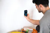 Une personne vérifie l'humidité des murs avec un humidimètre à côté des outils de peinture.