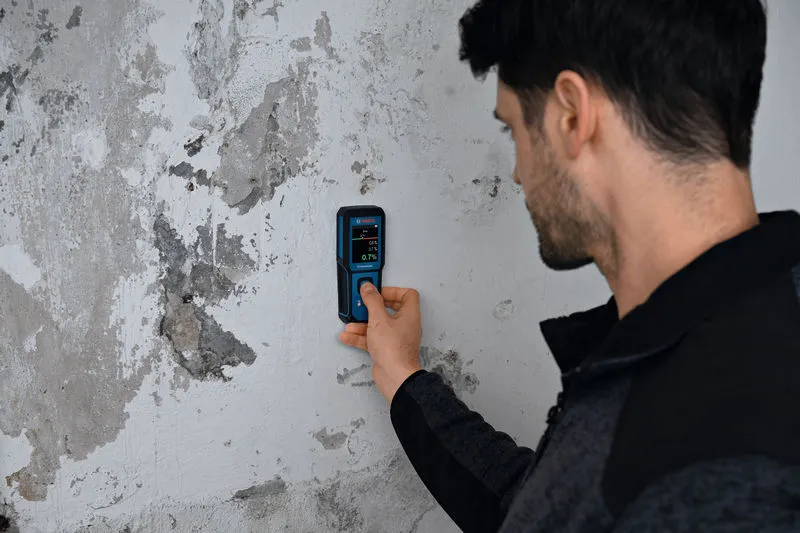 Une personne utilise un humidimètre pour vérifier l’humidité d’un mur endommagé.