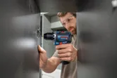Une personne portant un équipement de sécurité utilise une perceuse sans fil pour installer une charnière d’armoire.