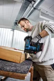 Une personne portant un équipement de sécurité utilise un pistolet à clous sans fil pour fixer des joints en bois.