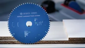 Lame de scie circulaire posée verticalement sur une table à côté de planches de bois stratifiées.