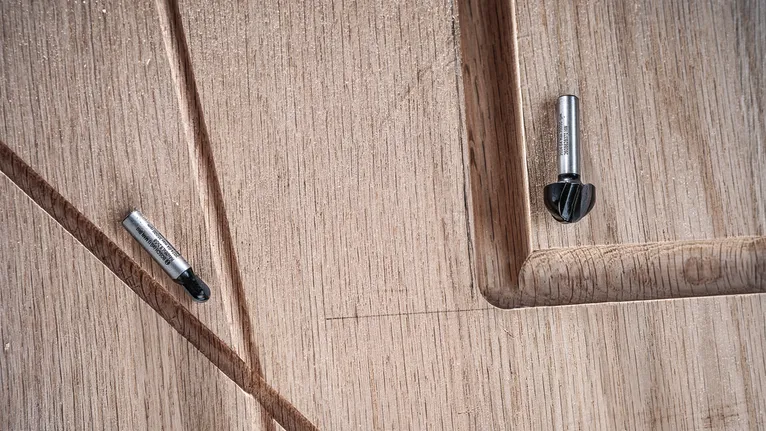 Deux mèches de toupie reposent sur une surface en bois sculptée avec des détails rainurés.