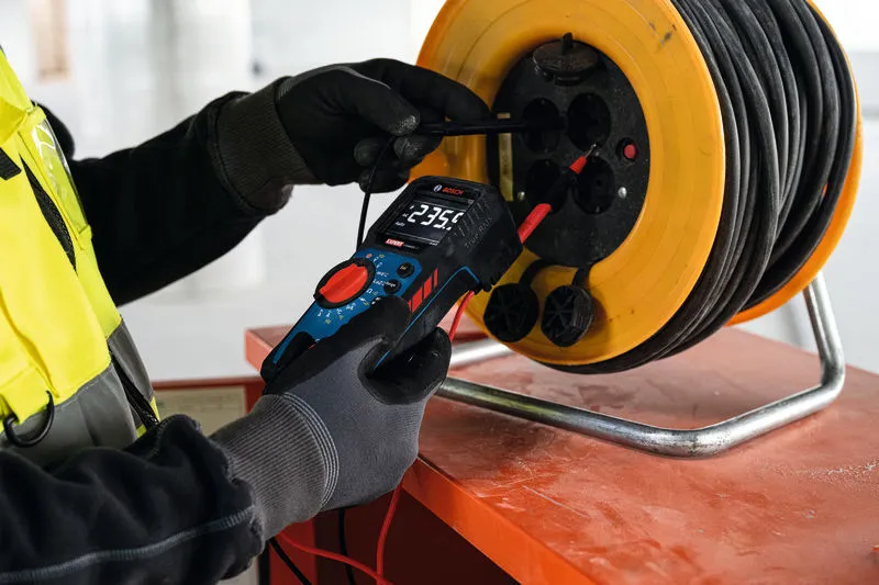 Une personne portant un équipement de sécurité utilise un multimètre numérique pour tester un enrouleur de câble d’alimentation.