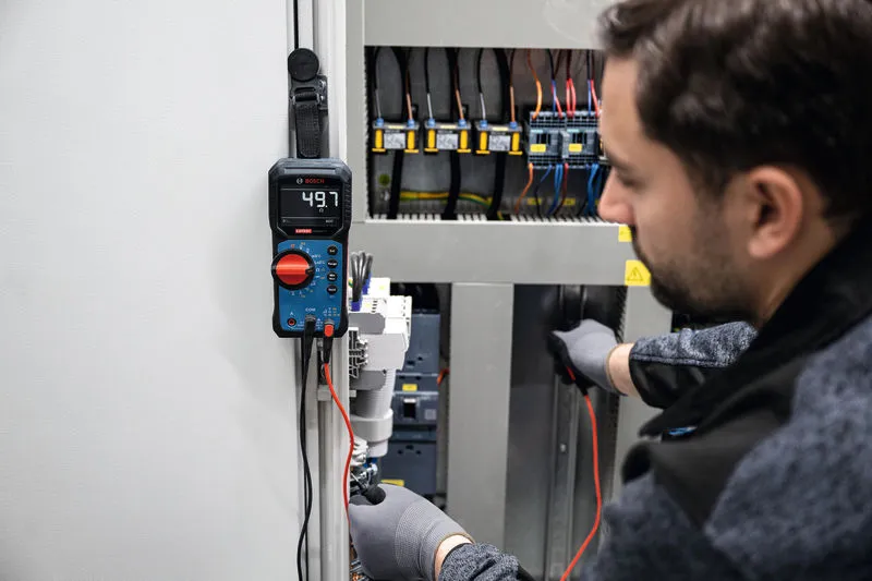 Une personne portant un équipement de sécurité utilise un multimètre numérique pour tester un panneau électrique.