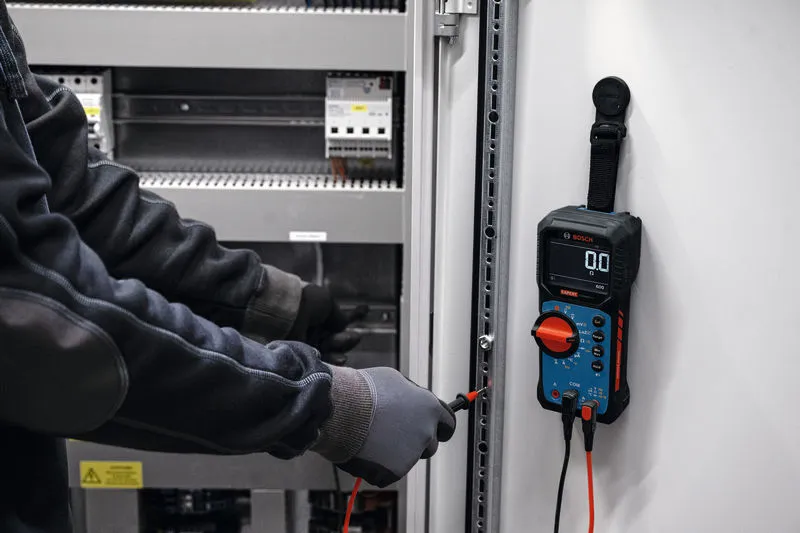 Une personne portant un équipement de sécurité utilise un multimètre numérique pour vérifier un panneau électrique.