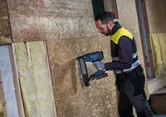 Une personne portant un équipement de sécurité utilise une agrafeuse à bois sans fil sur un mur OSB.