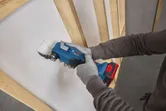 Une personne portant un équipement de sécurité découpe une ouverture carrée dans une cloison sèche à l’aide d’un outil multifonction.