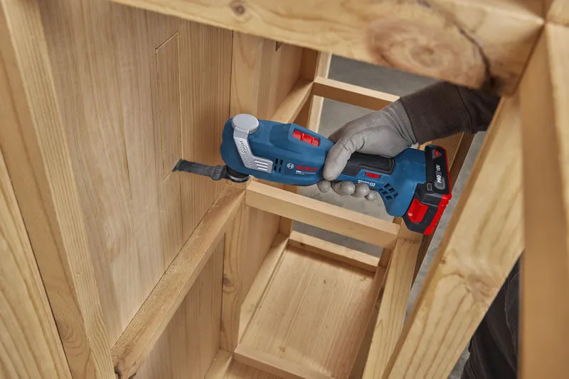 Une personne portant un équipement de sécurité découpe une ouverture rectangulaire dans une armoire en bois à l'aide d'un outil multifonction.