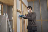 Une personne portant un équipement de sécurité utilise un outil multifonction pour couper des cloisons sèches.