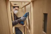 Une personne portant un équipement de sécurité utilise un outil multifonction pour couper du bois à l’intérieur d’une armoire.