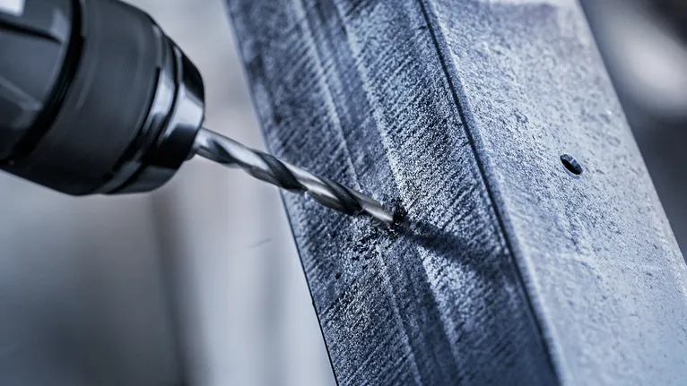 Une perceuse électrique crée un trou dans une poutre métallique.