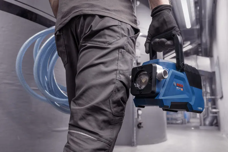 Une personne portant un équipement de sécurité transporte une pompe à vide portable bleue dans un environnement industriel.
