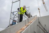Une personne portant un équipement de sécurité utilise un outil électrique sur un escalier en béton sur un chantier de construction.